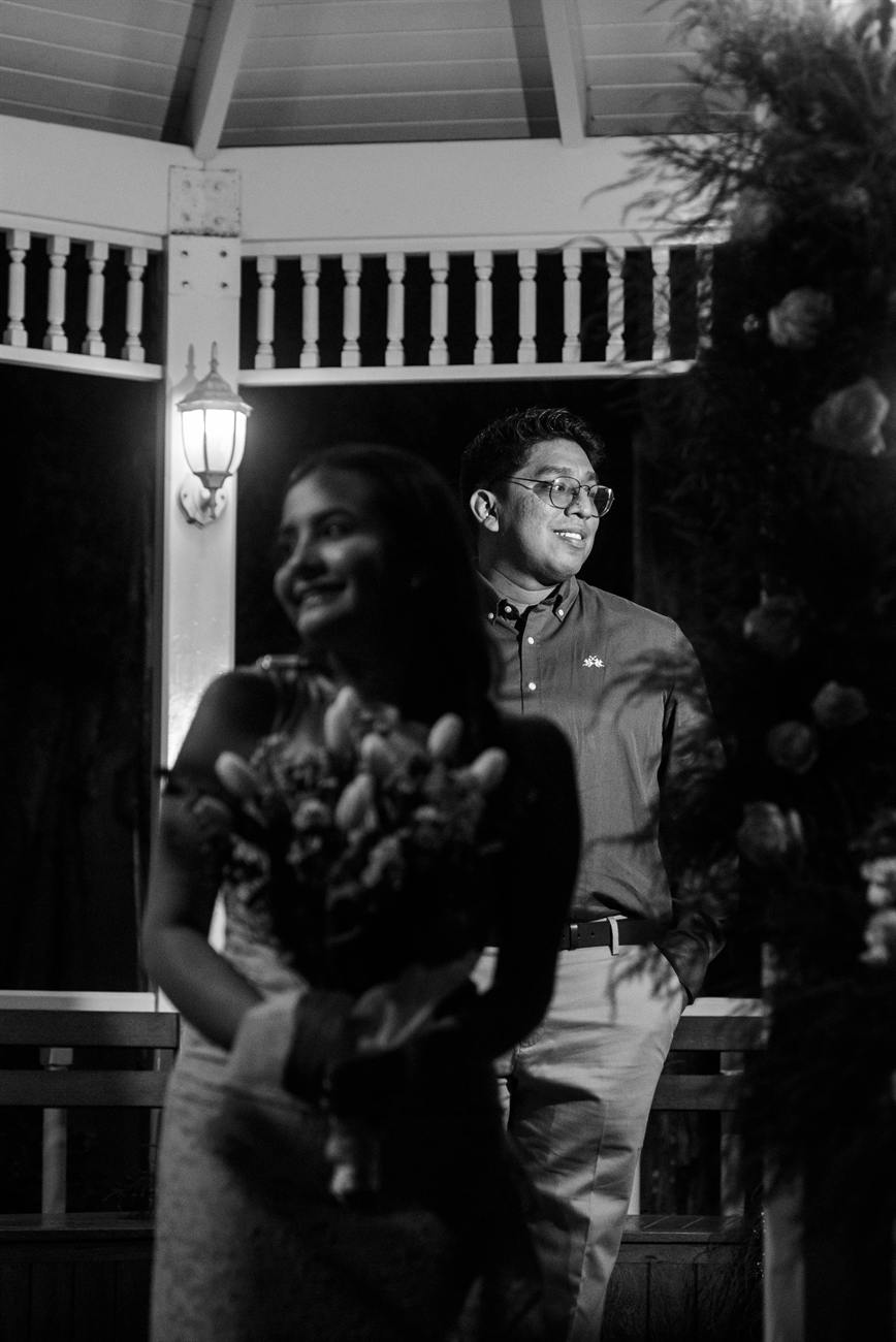 Retrato en blanco y negro de Angie con el ramo y Iván detrás, sonriendo.